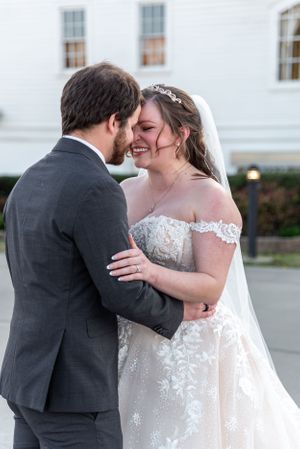 Romantic moment between newlyweds in formal attire outside white building.