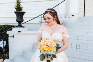 A white wedding dress and yellow bouquet are showcased against classic white architecture.