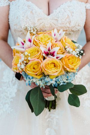 Vibrant yellow roses and pink lilies make up an elegant bridal bouquet against a lace wedding dress.