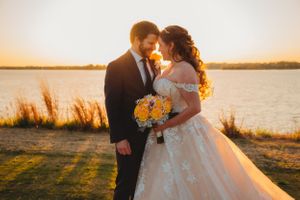 Sunset waterfront wedding portrait with yellow bouquet and flowing dress.