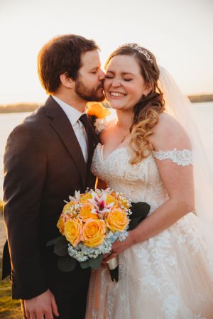 Wedding couple shares intimate moment at sunset while holding bright yellow and pink bouquet.