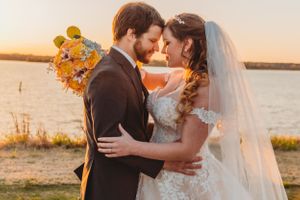A romantic sunset wedding photo shows a couple embracing by the water with golden sunlight and yellow flowers.