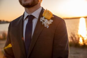 Yellow rose boutonniere and navy tie detail on suit jacket at sunset by the water.