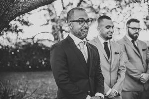 A black and white portrait of groomsmen in formal attire waiting during ceremony.