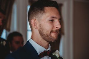 A groom in a dark suit and burgundy tie with boutonniere during the wedding ceremony.