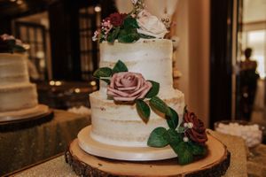 Elegant white wedding cake decorated with dusty rose flowers and green foliage on a wooden stand.