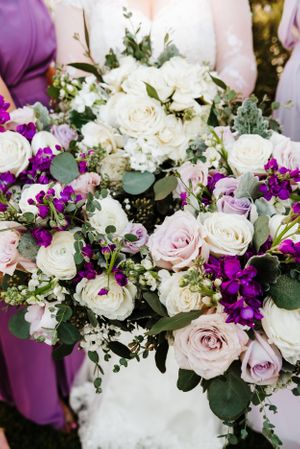A stunning wedding bouquet with purple and white roses, mixed with greenery.