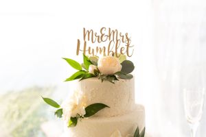 White wedding cake decorated with peach flowers and gold 'Mr & Mrs' topper against light background.