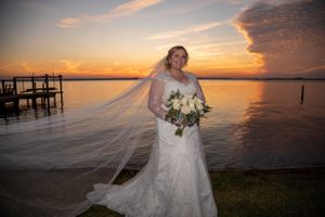 A sunset wedding portrait by a dock with flowing veil and bouquet.