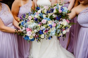 Bridesmaids in lavender dresses hold beautiful blue and purple wedding bouquets.