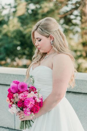 A bride in a sweetheart neckline dress gazes down at her pink floral bouquet.