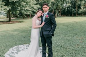 Newlyweds share intimate moment on stone pathway surrounded by lush greenery.