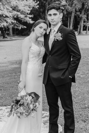 Classic black and white portrait of newlyweds in formal wedding attire outdoors.