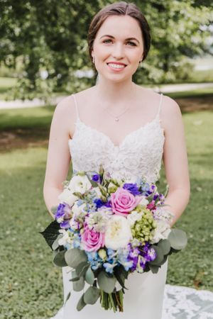 Radiant bride in lace wedding dress holds vibrant bouquet of pink, purple, and white flowers.
