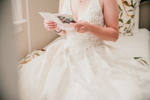 Close-up view of a bride in a white lace dress reading a letter while sitting.