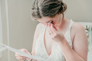 Emotional bride in white dress reads a note while getting ready.