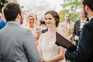 Bride in lace dress listens intently during outdoor wedding ceremony.