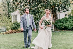 A newlywed couple strolls through a garden setting, with the bride's dress flowing in the breeze.