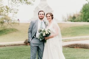 A wedding couple poses for a portrait on their special day with greenery and architecture in the background.