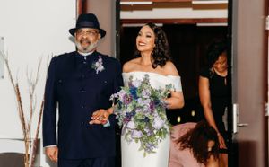 A bride walks down the aisle with her escort at an indoor ceremony.