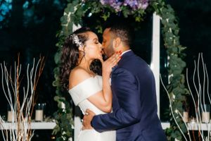A couple kisses under a floral arch during their wedding ceremony.