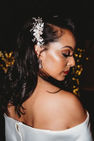 Close up profile of a bride wearing an elegant hair accessory against dark background with bokeh lights.