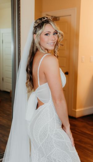 Bride in fitted lace wedding dress with veil poses showing open back detail.