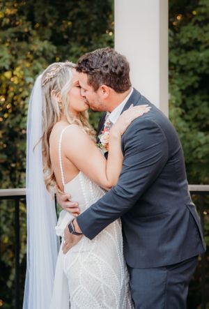 Romantic wedding couple sharing intimate kiss under white gazebo.