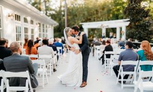Outdoor wedding ceremony with couple dancing among white chairs and guests.