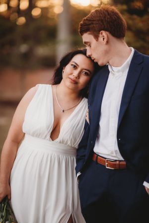 A romantic couple shares an intimate moment in formal attire at sunset.