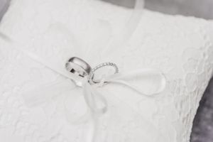 Wedding rings tied with white ribbon rest on delicate lace pillow.