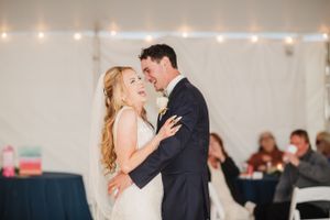 A couple shares their first dance together at their wedding reception with string lights and guests in the background.
