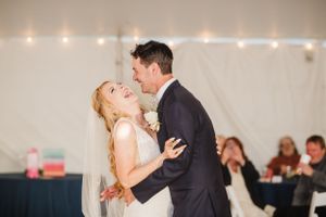 A joyful couple shares their first dance at their wedding reception with twinkling lights in background.