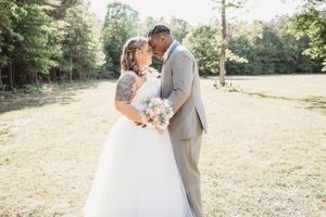 A couple embraces in a romantic wedding photo in a sunlit field.