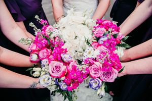 Multiple hands hold a stunning wedding bouquet featuring pink and white roses with bright fuchsia accents.