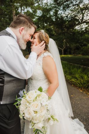 A tender wedding moment captured as newlyweds share an intimate kiss while holding a white bouquet.
