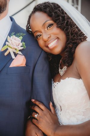 Close-up shot of a radiant bride in a lace gown with a pink rose boutonniere detail.