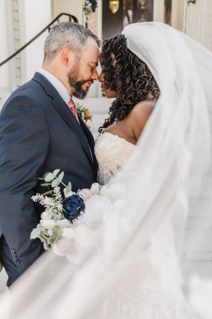 A tender moment between newlyweds with a floral bouquet and flowing veil.