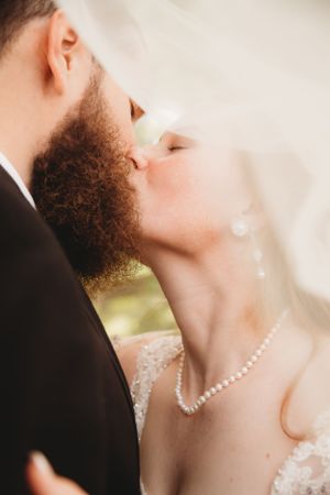 Close-up shot of romantic couple sharing intimate kiss with elegant pearl necklace detail.