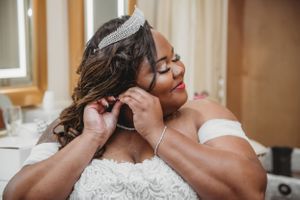 Close up of someone adjusting jewelry while wearing bridal gown near window.