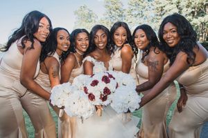 Bridesmaids in champagne dresses hold white and red floral bouquets outdoors.