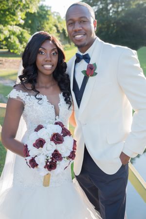 Wedding couple poses outdoors with red and white rose bouquet.