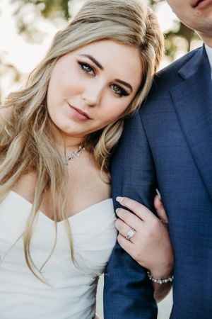 Close-up portrait of a bride in white dress wearing delicate necklace next to groom in navy suit.