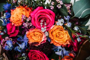 Vibrant wedding bouquet with orange and pink roses accented with blue flowers and greenery.