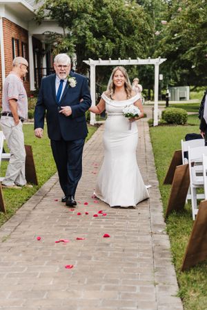 Wedding processional on a brick path with rose petals scattered on the ground.