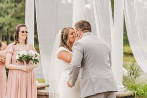 Wedding ceremony under white draping with bridesmaid in pink dress watching.