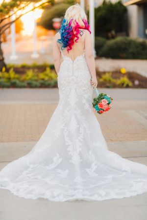 Elegant lace wedding dress with long train photographed from behind with colorful hair and bouquet.