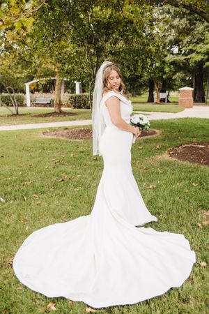 Bride in flowing white mermaid wedding gown poses on grass with dramatic train spread out.