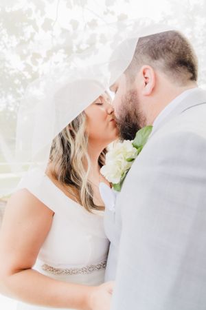 Romantic wedding photo of couple in light gray suit and white dress sharing a tender kiss.