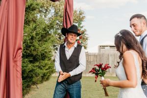 Western-style wedding ceremony with groom in cowboy hat and vest at an outdoor venue.